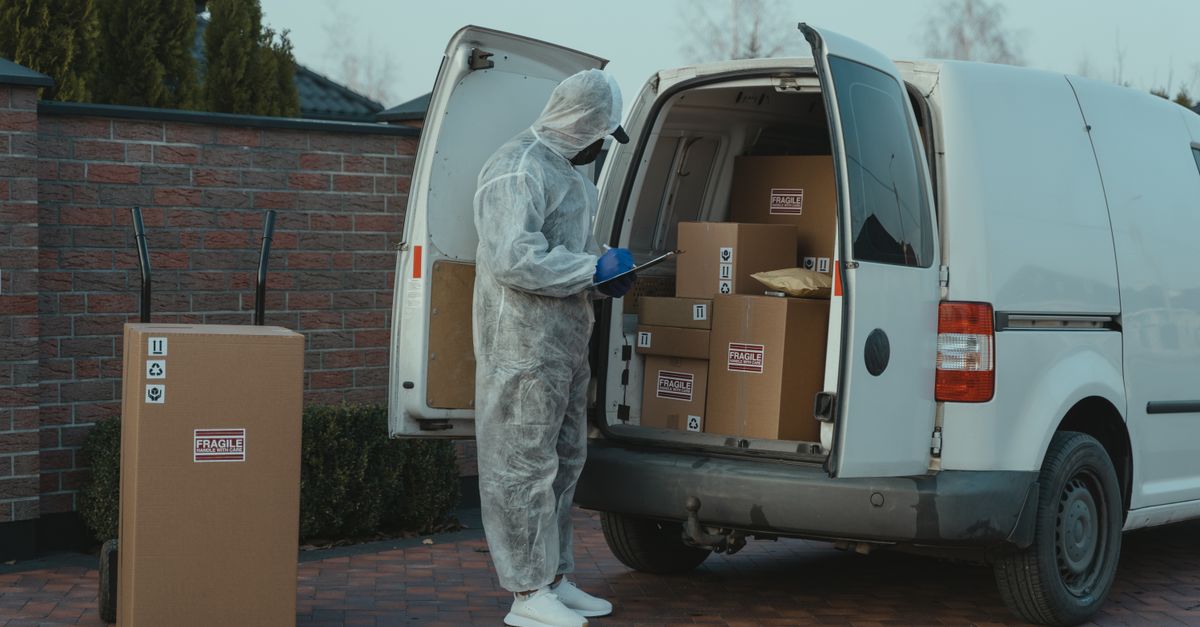 Delivery worker wearing PPE loads packages into a van with fragile labels for shipment.