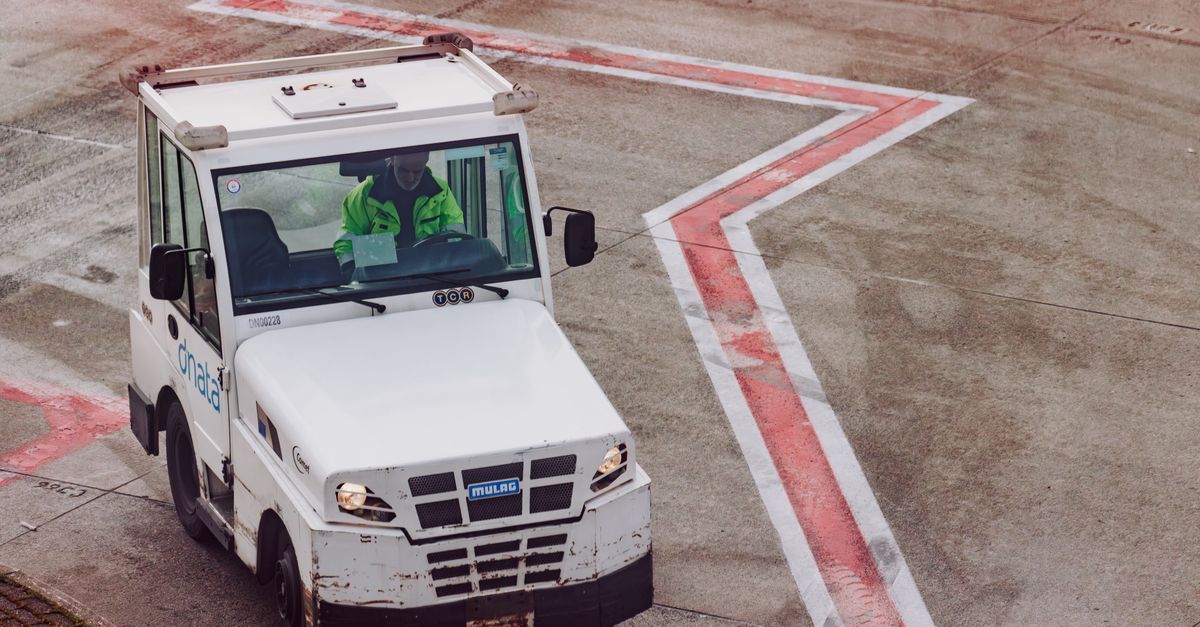 A ground crew vehicle navigates the airport tarmac during daytime operations.